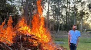Byron Miller standing next to a large fire in his backyard with a horse paddock in the back ground