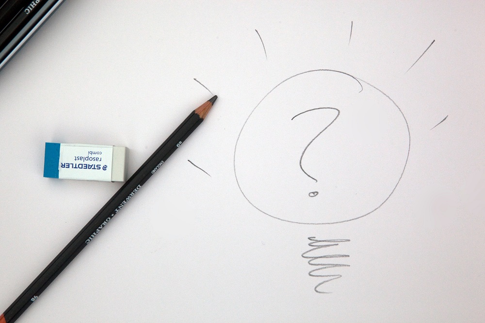 Big question mark drawn inside a light bulb on a white sheet with pencil and eraser