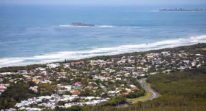 Aerial view of a coastal town along the Sunshine Coast, showcasing the vibrant ocean and surrounding landscape