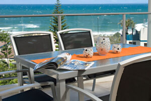An image of a balcony featuring a table and chairs, with a stunning ocean view stretching out beyond.