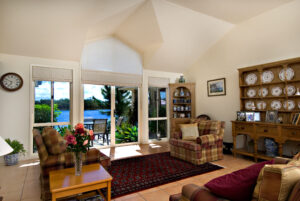 A warm living room with plaid chairs, a wooden cabinet, and large windows showing a peaceful lake.