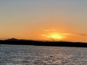 A photo of The sun sets over the Sunshine coast region, casting warm colors across the sky and shimmering on the waves.